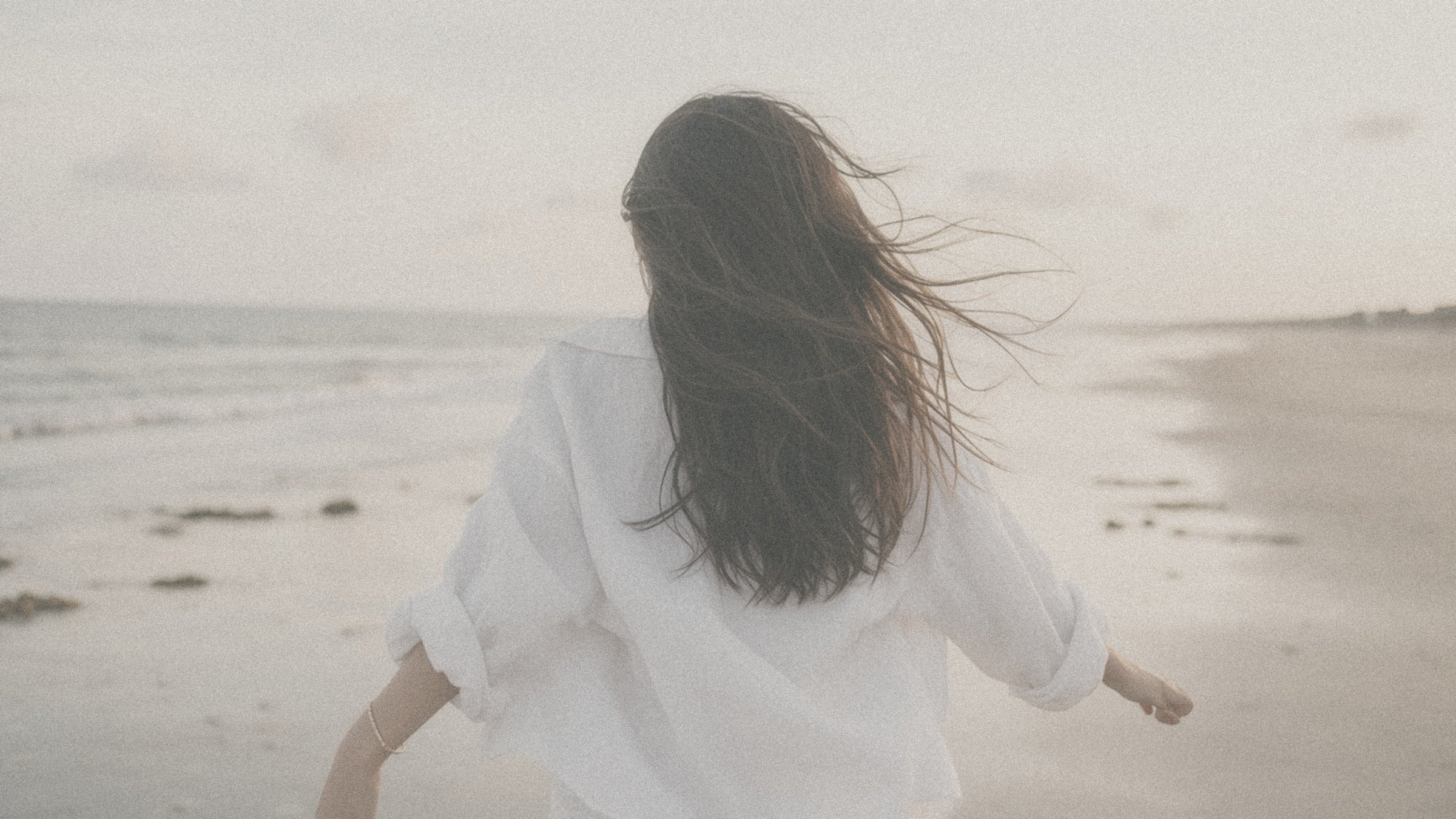 Chiara running along the shoreline in a white linen shirt
